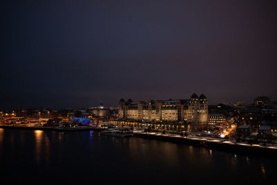 Illuminated buildings by river against sky at night