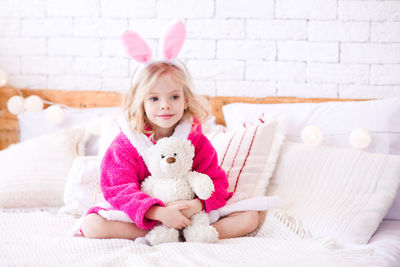 Cute girl with teddy bear sitting on bed