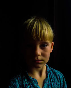 Close-up portrait of blond boy against black background