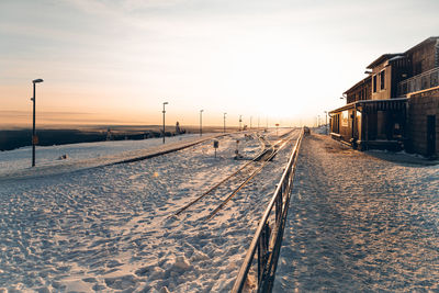 Railroad tracks on snow covered street against sky during sunset