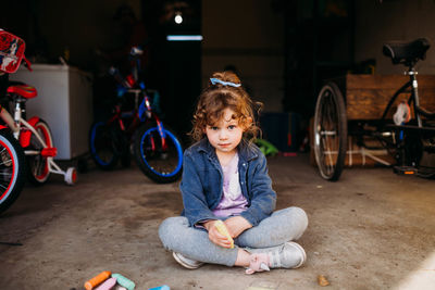 Young girl sitting in garage coloring with chalk in spring