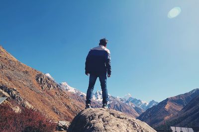 Rear view of man standing on rock against clear blue sky