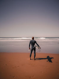 Full length of woman with surfboard standing at beach against clear sky