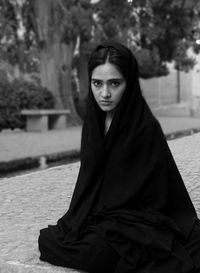 Portrait of young woman sitting on footpath