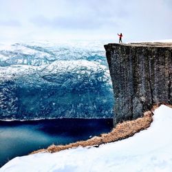 Person on snowcapped mountain by sea against sky