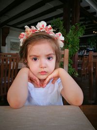 Portrait of cute girl wearing floral wreath while sitting at cafe