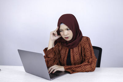 Young woman using phone while sitting on wall