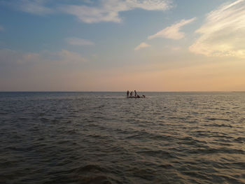 People in sea against sky during sunset