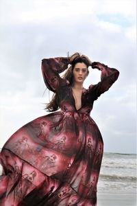 Portrait of woman with arms raised standing at beach against sky