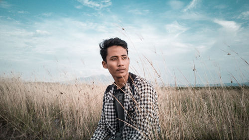 Portrait of young man standing on field against sky