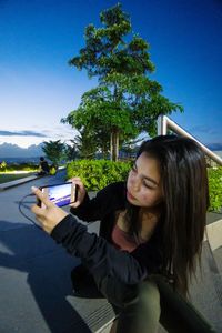 Man photographing while using smart phone by tree