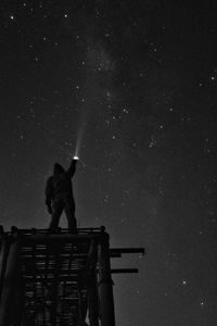 Low angle view of silhouette man holding illuminated flashlight against star field at night