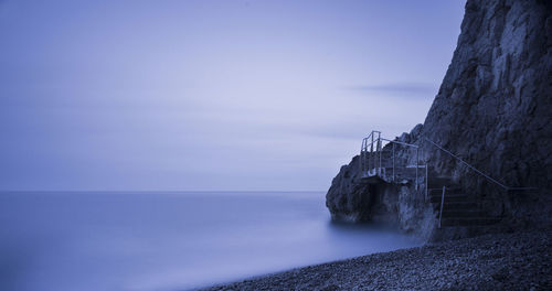 Steps on cliff by sea against cloudy sky