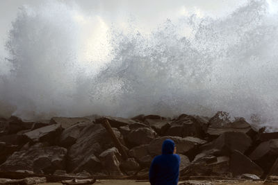 Rear view of woman standing on rock against sky