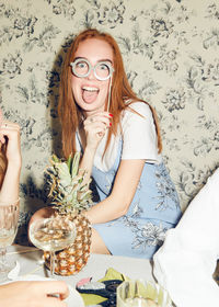 Portrait of young redhead woman holding prop while sitting amidst friends during dinner party at home