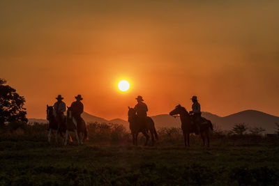 People riding horses on field against sky during sunset