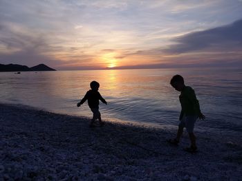 Silhouette men on beach against sky during sunset