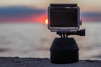 Close-up of camera against sky during sunset