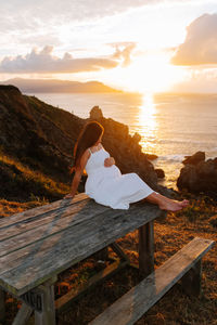 Woman sitting on bench looking at sea during sunset