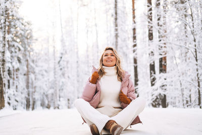 Portrait of smiling blonde woman with blonde hair in winter clothes in snowy winter forest