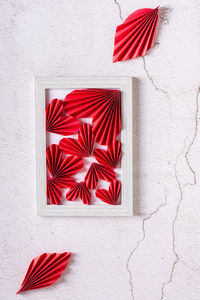Red paper diy hearts in an empty photo frame and leaves on a concrete background. vertical view