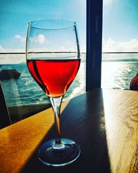 Red wine in glass on table by sea against sky