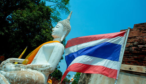 Low angle view of buddha statue and thai flag