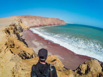 Man standing on rock by sea against sky