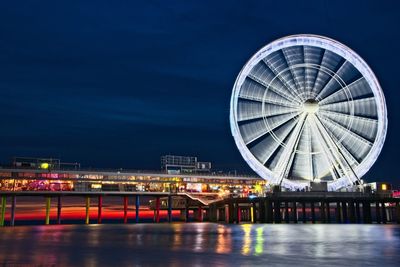 Illuminated ferris wheel in city against sky at night