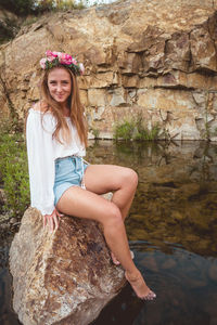 Portrait of a smiling young woman standing on rock by the lake