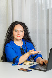 Portrait of young woman using phone while sitting on table