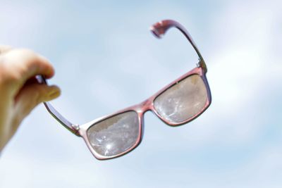 Close-up of hand holding sunglasses against sky