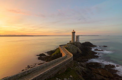 Lighthouse by sea against sky during sunset