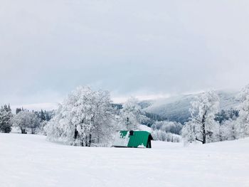 Single house with green roof surrounded by heavy snow and trees covered in snow with mountains