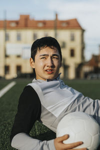Male teenager athlete with soccer ball looking away in sports field