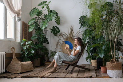 Young relaxed dreamy woman using paper fan while relaxing in beautiful refreshing home garden