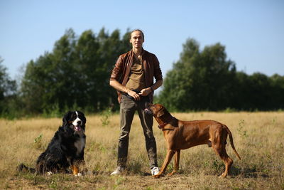 Full length of man playing with dog while standing on grass against sky