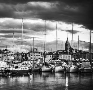 Sailboats moored at harbor against cloudy sky