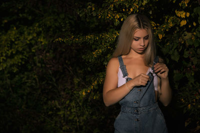 Young woman getting dressed standing against plants