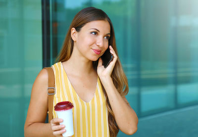 Smiling young woman using phone while standing against building