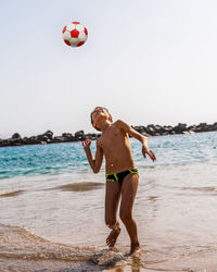 Young boy playing with a soccer ball on the beach by the sea - summer vacation concept