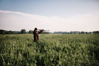 Person aiming with gun amidst grass on field