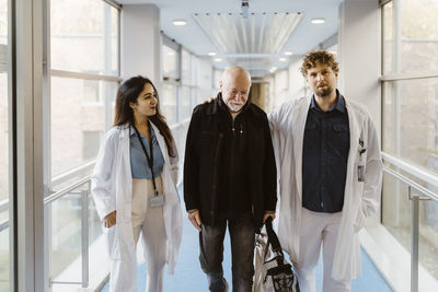 Smiling female doctor walking by colleague with patient in corridor hospital