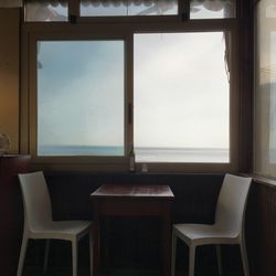 Empty chairs and table against sky seen through window