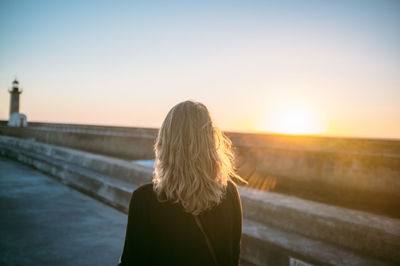 Rear view of woman standing against clear sky during sunset