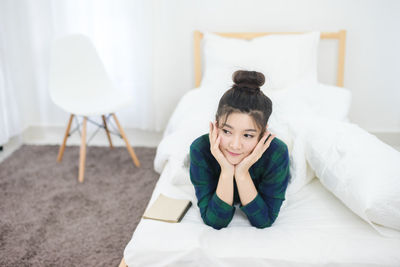 Woman with hand on chin lying on bed at home