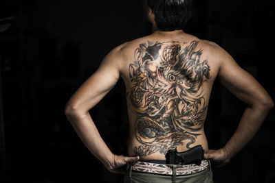 Rear view of tattooed man with gun
