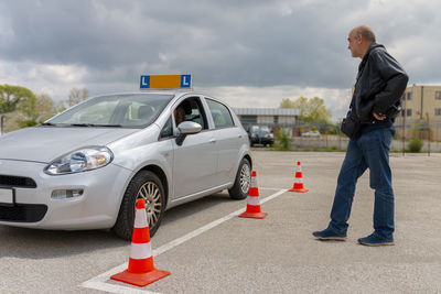 Driving instuctor watching teenage girl practising driving on the polygon with cones at the day