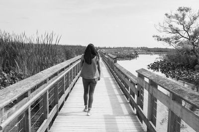 Rear view of woman on footbridge against sky