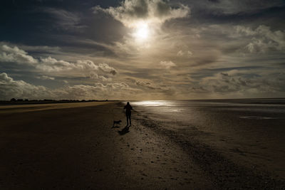 Man walking on beach against sky during sunset